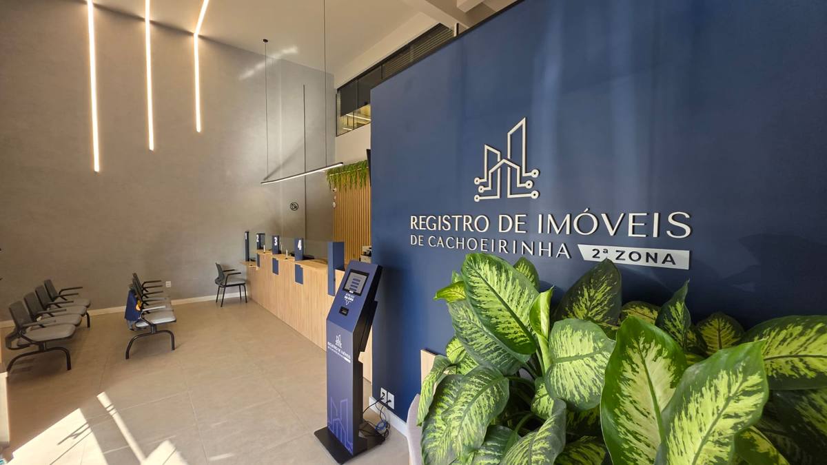 Recepção do 2º Registro de Imóveis de Cachoeirinha, com a parede azul que leva o nome do cartório, o totem de senhas e os guichês de atendimento ao fundo